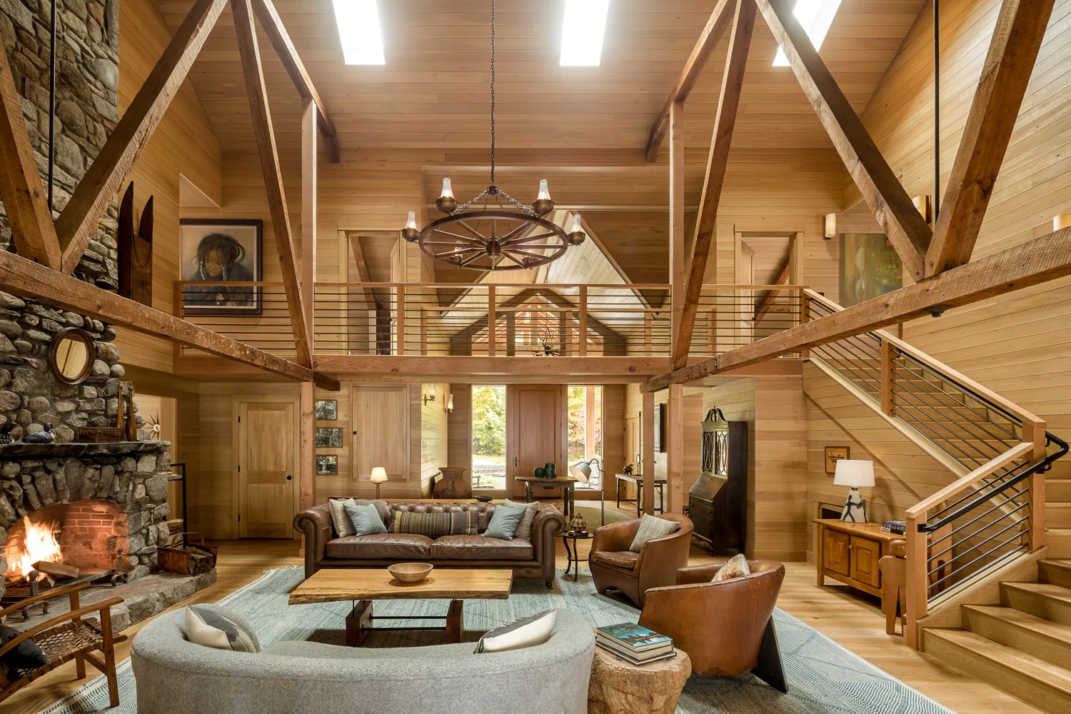 Timber frame great room with exposed beams, stone fireplace, and custom loft railing